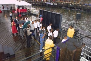 A TV camera crew films a children's choir in white shirts performing on the dock at South Street Seaport, September 10, 2001, photographed by Jack Hartzman.