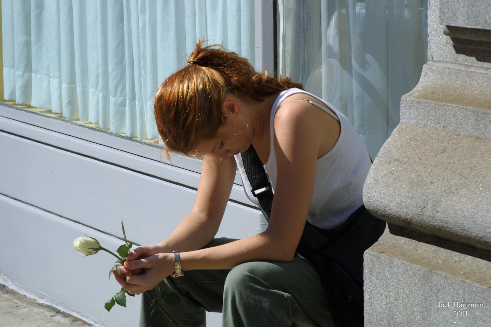 A woman sits quietly holding a single white rose near Chanterelle in Tribeca on September 11, 2001, photographed by Jack Hartzman.